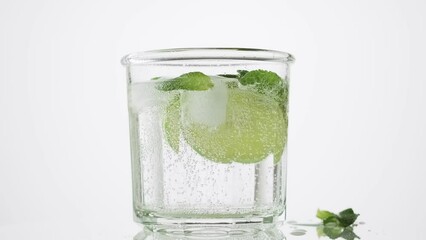 Wall Mural - Soda water with lime, mint and ice in the glass on the white background, rotate, 4k. Fresh lime detox water with bubbles.