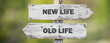 © Jon Anders Wiken - opposite signs on wooden signpost with the text quote new life old life engraved. Web banner format.