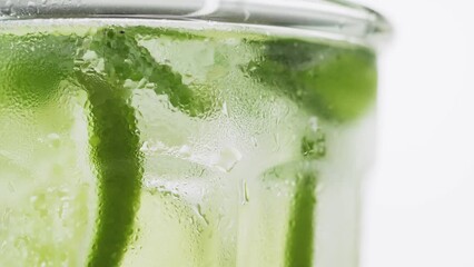 Wall Mural - Soda water with lime, mint and ice mixing with drinking straw in the wet glass on the white background, rotate, macro shot, 4k. Fresh lime detox water with bubbles.