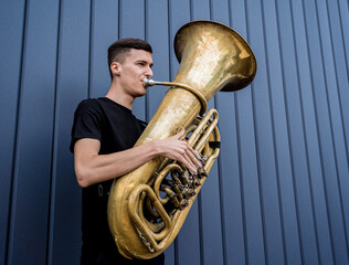 Young street musician playing the tuba near the big blue wall