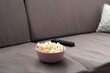 Bowl with popcorn and tv remote control on sofa