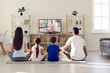 © Studio Romantic - Young family with children practice yoga and meditate together at home in front of TV screen. Mom, dad, daughter and son sit in lotus position on living room floor and watch online practice. Rear view