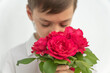 © Anna - Boy in white shirt with closed eyes is hiding his face in bouquet of red roses on white background. Greetings concept. Happy birthday, valentines day, mothers day