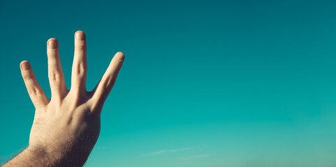 Male hand showing or doing number four gesture on blue summer sky background. Man gesturing number 4 in sign language. Counting down, four fingers up concept idea. Rabia sign. Copy space for text.