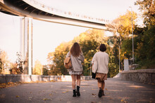 Back View Of Two Teenage Girls Walking In Park In City In Autumn