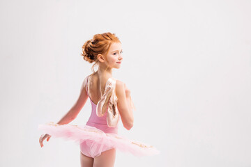 Portrait of a little tender red-haired girl in a pink tutu with pointe shoes, dreaming of becoming a ballerina