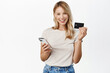 Beautiful smiling woman showing credit card while paying with mobile phone app, using smartphone, shopping online, purchase smth,white background