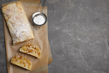 Delicious apple strudel with almonds and powdered sugar on grey table, flat lay. Space for text