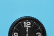 Stylish analog clock hanging on light blue wall, space for text