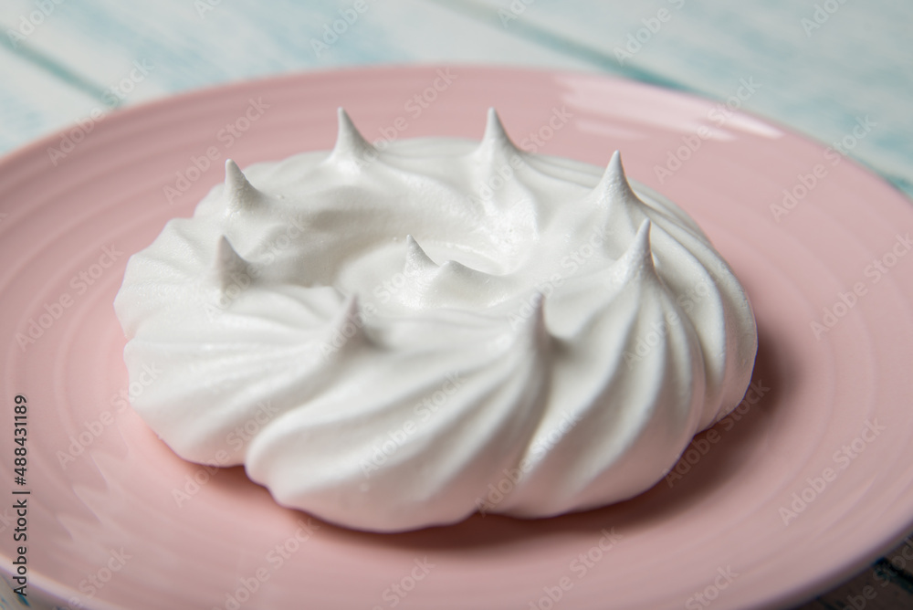 One large meringue on a pink saucer. Home confectionery. Old retro white and blue table.