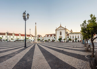 Wall Mural - Sunrise in the Marquês de Pombal square in Vila Real de Santo António, Algarve, Portugal, with the obelisk in the center of the square and the old houses and church in the background.