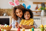 Fototapeta Panele - Happy african american family: mother teaching happy little kid soon to decorate Easter eggs while sitting in kitchen
