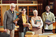 Diverse Group Of People Holding Books In Classic Library And Looking At Camera