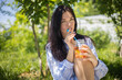 © kostikovanata - Portrait of happy young brunette woman posing drinking fresh fruit cocktail relaxing at summer park
