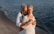 © MZaitsev - Romantic senior couple is embracing on seashore. Man hugs woman from behind.
