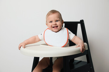 Cute little baby wearing bib in highchair on white background