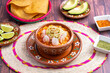 Traditional mexican food. Red pozole soup with chicken accompanied with avocado, lettuce, onion, radish, lemon, chili and crispy corn tortillas also known as tostadas on a wooden background.