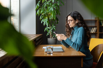 Woman writer, student, copywriter or freelancer use smartphone at workplace. Busy female businesswoman read message in mobile phone working remotely from coworking space. Digital technology concept