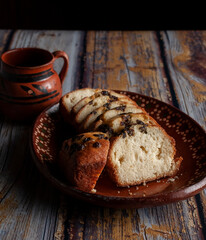 Dark food photography, black coffee in a Mexican clay jar with sweet bread and raisins slices, on an old rustic wooden table. side view vertical image of Dark Food Photography. 