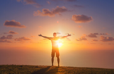 Wall Mural - Man relaxing in a field enjoying nature with arms outstretch up to the sunrise. Feelings of hope, worship  and happiness 