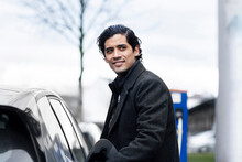 Smiling Man With Black Hair Standing By Electric Car