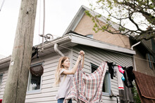 Girl Hanging Clothes On Rope Outside House