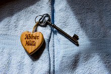 Old House Key On Heart Shaped Key Ring Lying On Top Of Pastel Blue Towels