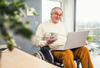 © Westend61 - Smiling disabled senior man holding coffee cup talking on video call through laptop at home