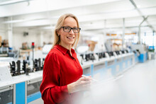 Smiling Blond Businesswoman Wearing Eyeglasses Holding Tablet PC In Factory