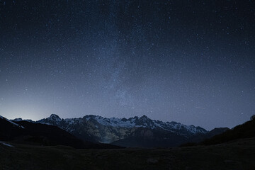 Wall Mural - a scenic view of a field against a snowy mountain under the starry night sky