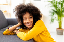 Smiling Young Woman Leaning On Sofa Sitting In Living Room