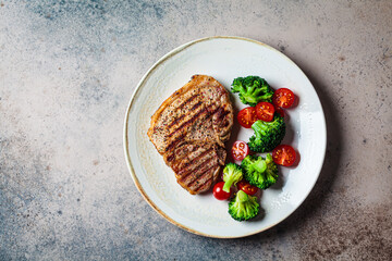 Canvas Print - Grilled pork steak with broccoli and tomatoes on plate, dark background.