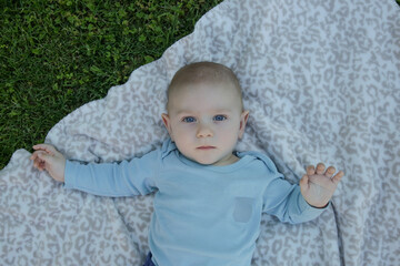 Portrait of cute blue eyed baby boy laying down on the blanket on the grass, top view