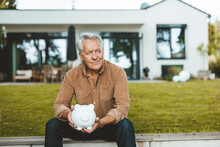 Senior Man With Piggy Bank Sitting At Backyard