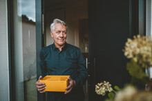 Smiling Senior Man With White Hair Holding Package At Doorway