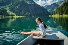 Girl Sitting On Bow Of Rowboat Dipping Feet In Lake