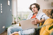 © Westend61 - Young man with brown hair using laptop sitting on sofa at home