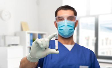 Wall Mural - healthcare, coronavirus and medicine concept - doctor in blue uniform, face protective medical mask, goggles and gloves with blood in test tube over medical office at hospital background