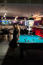 Pretty Woman Holding Cue And Sits On The Edge Of Billiard Table