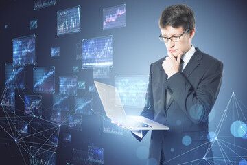 Poster - Attractive young european businessman using laptop with creative forex charts on blurry background. Trade and economy concept. Double exposure.