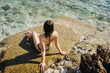 © diignat - Happy young woman enjoying freedom on vacation while sitting on the coast rocks enjoying sea and blue sky view