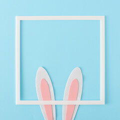 Wall Mural - Happy Easter minimal concept. Bunny rabbit ears and white frame on pastel blue background, flat lay.