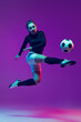 © master1305 - Dynamic portrait of female soccer player practicing with football ball isolated on purple studio background in neon light. Sport, action, motion, fitness