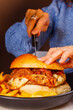 © Vincenzo VAD - Panino da pub con Hamburger di carne, provola affumicata, pulled pork e bacon croccante mentre viene tagliato con un coltello da una cliente