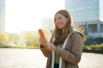 Wall Mural - Young woman typing on her smartphone in city on spring time