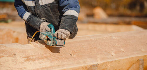 Poster - Industrial work carpenter grinds log with electric jointer, construction frame building site of house made of wood