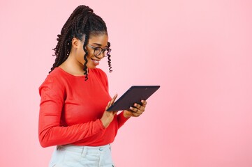 Young american student girl with curly african hair holding digital tablet and smiling standing over isolated pink background with copy space for text, logo or advertising.