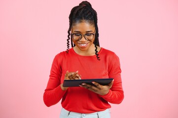Young american student girl with curly african hair holding digital tablet and smiling standing over isolated pink background with copy space for text, logo or advertising.
