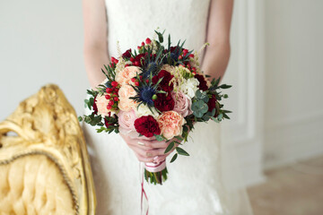 A bride with a wedding bouquet of roses and carnations on the background of a wedding dress