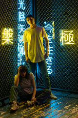 Wall Mural - Young couple in white t-shirts stand against the background of a metal grid with neon symbols.